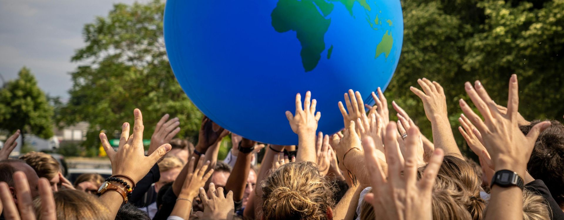 A vibrant scene of people raising hands to a large inflatable globe at a public event in Berlin.