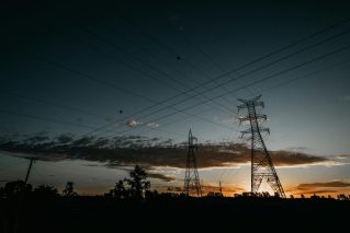 Electricity towers silhouetted against a vibrant sunset sky with power lines stretching across.